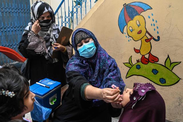 A healthcare worker (C) administers polio drops to a school child during a door-to-door poliovirus eradication campaign in Lahore on April 13, 2026. (Photo by Arif ALI / AFP)