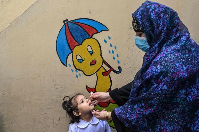 A healthcare worker administers polio drops to a school child during a door-to-door poliovirus eradication campaign in Lahore on April 13, 2026. (Photo by Arif ALI / AFP)