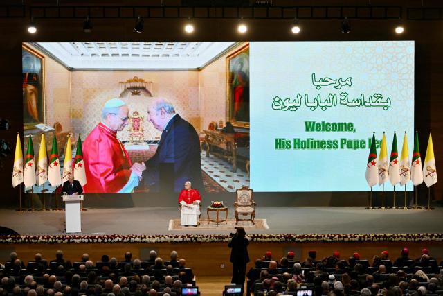 Pope Leo XIV listens to Algeria's President Abdelmadjid Tebboune during a meeting with the civil society and the diplomatic corps at the “Djamaa el Djazair” Conference Center  on April 13, 2026. Pope Leo XIV embarks today on an 11-day visit to Algeria, Cameroon, Angola and Equatorial Guinea for his first major international trip since becoming pontiff last year. (Photo by Alberto PIZZOLI / AFP)