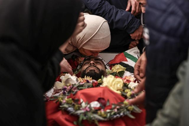 EDITORS NOTE: Graphic content / A relative of 23-year-old Ali Majed Hamadneh kisses him farewell during his funeral in the village of Deir Jarir, northeast of the city of Ramallah in the Israeli-occupied Palestinian West Bank on April 13, 2026. The Palestinian health ministry reported on April 12, 2026, that Israeli settlers shot dead Hamadneh in the occupied West Bank, while the military said a soldier had opened fire during a "violent riot". Violence in the West Bank, which Israel has occupied since 1967, has risen sharply since the October 7, 2023 Hamas attack on Israel triggered the Gaza war. (Photo by Zain JAAFAR / AFP)