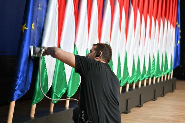 A staff member irons an EU-flag beside Hungarian flags prior a press conference at the HUNGEXPO Congress and Exhibition Center in Budapest, Hungary, on April 13, 2026. The party of conservative Peter Magyar won a two-thirds parliamentary majority in Hungarian elections in a clear defeat for nationalist long-time Prime Minister Viktor Orban, according to near-complete results. (Photo by Attila KISBENEDEK / AFP)