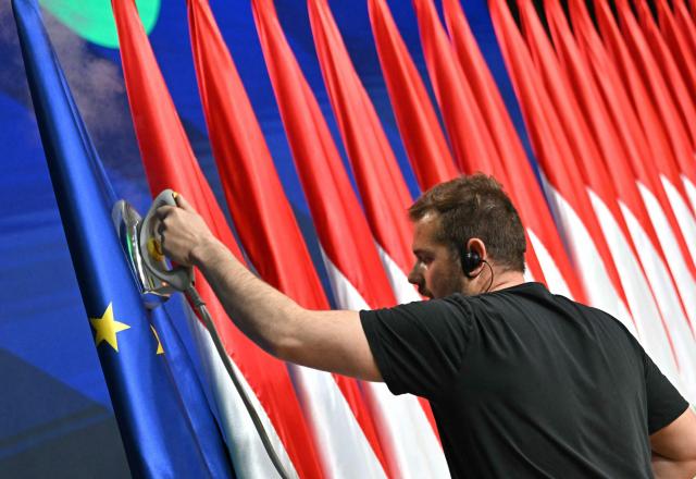 A staff member irons an EU-flag beside Hungarian flags prior a press conference at the HUNGEXPO Congress and Exhibition Center in Budapest, Hungary, on April 13, 2026. The party of conservative Peter Magyar won a two-thirds parliamentary majority in Hungarian elections in a clear defeat for nationalist long-time Prime Minister Viktor Orban, according to near-complete results. (Photo by Attila KISBENEDEK / AFP)