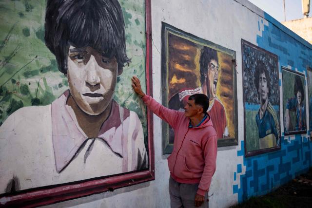 A man touches a mural depicting the late football star Diego Maradona in his hometown neighborhood Villa Fiorito, in Buenos Aires province, Argentina, on April 9, 2026. The second trial over the death of football star Diego Maradona begins on April 14, 2026, after the first one, which took place last year, was annulled when it was discovered that one of the judges was taking part in a clandestine documentary about the proceedings. (Photo by TOMAS CUESTA / AFP)