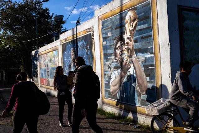People walk past past murals depicting the late football star Diego Maradona in his hometown neighborhood Villa Fiorito, in Buenos Aires province, Argentina, on April 9, 2026. The second trial over the death of football star Diego Maradona begins on April 14, 2026, after the first one, which took place last year, was annulled when it was discovered that one of the judges was taking part in a clandestine documentary about the proceedings. (Photo by TOMAS CUESTA / AFP)