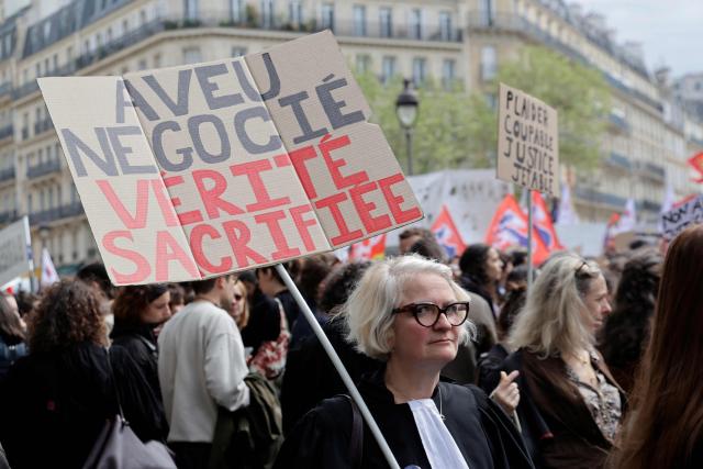 A lawyer holds a placard reading "A confession negotiated, the truth sacrificed" during a demonstration against the Darmanin law, which intends to shorten trial times, in Paris on April 13, 2026. The criminal justice reform promoted by France's Justice Minister arrives on April 13 in the Senate chamber, accompanied by a mobilization of lawyers criticizing a reform that will be "to the detriment of the rights of the defense and of victims". (Photo by Ludovic MARIN / AFP)