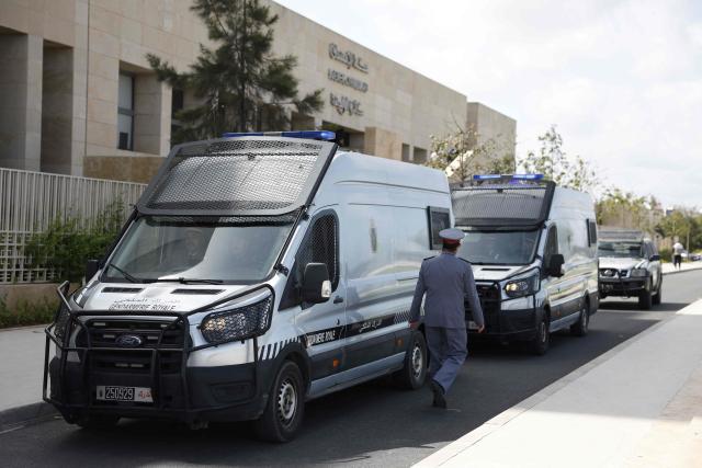 A police officer walks past police vans believed to be transporting Senegalese detainees outside the Rabat Court of Appeal on April 13, 2026. A Moroccan court on February 19 sentenced 18 Senegalese football fans to prison terms ranging from three to 12 months over hooliganism charges. The group had been in pre-trial detention since January 18, the day of the heated AFCON final in which Morocco lost to Senegal 1-0 on home turf, after some Senegalese supporters attempted a pitch invasion while others threw objects onto the field. (Photo by Abdel Majid BZIOUAT / AFP)