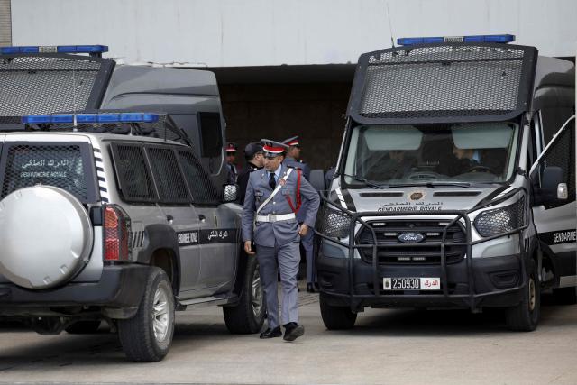 A police officer walks past police vans believed to be transporting Senegalese detainees outside the Rabat Court of Appeal on April 13, 2026. A Moroccan court on February 19 sentenced 18 Senegalese football fans to prison terms ranging from three to 12 months over hooliganism charges. The group had been in pre-trial detention since January 18, the day of the heated AFCON final in which Morocco lost to Senegal 1-0 on home turf, after some Senegalese supporters attempted a pitch invasion while others threw objects onto the field. (Photo by Abdel Majid BZIOUAT / AFP)