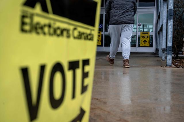 A perso walks past a placard directing voters outside of a polling station, in Terrebonne, Quebec, Canada, on April 13, 2026. Canada is holding by-elections in three federal electoral districts to fill vacancies in the Parliament, which could give Prime Minister Mark Carney's Liberal Party a majority government. (Photo by ANDREJ IVANOV / AFP)