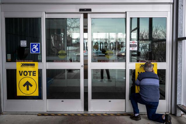 A volunteer writes polling station numbers on a sign informing voters where to vote outside a polling station, in Terrebonne, Quebec, Canada, on April 13, 2026. Canada is holding by-elections in three federal electoral districts to fill vacancies in the Parliament, which could give Prime Minister Mark Carney's Liberal Party a majority government. (Photo by ANDREJ IVANOV / AFP)