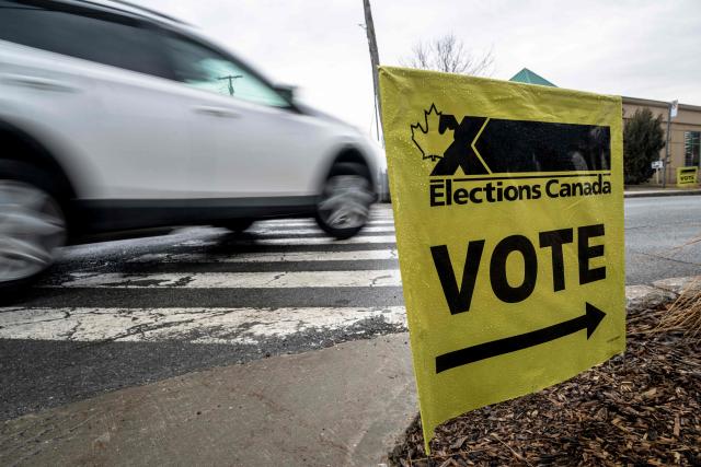 A placard directs voters outside of a polling station, in Terrebonne, Quebec, Canada, on April 13, 2026. Canada is holding by-elections in three federal electoral districts to fill vacancies in the Parliament, which could give Prime Minister Mark Carney's Liberal Party a majority government. (Photo by ANDREJ IVANOV / AFP)