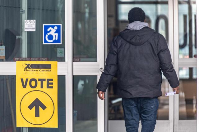 A person walks past a placard directing voters outside of a polling station, in Terrebonne, Quebec, Canada, on April 13, 2026. Canada is holding by-elections in three federal electoral districts to fill vacancies in the Parliament, which could give Prime Minister Mark Carney's Liberal Party a majority government. (Photo by ANDREJ IVANOV / AFP)