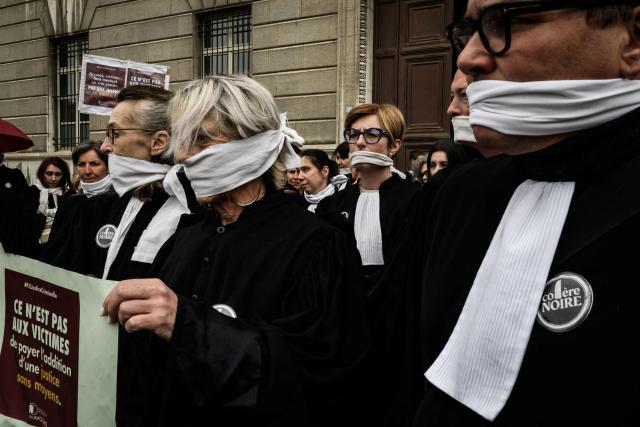 Lawyers gather with their mouths taped shut, in front of the Chambery courthouse, during a demonstration by lawyers against the "SURE" (Useful, Fast and Effective Sentencing) draft bill, in particular its proposal to introduce plea bargaining in criminal matters, as the French Senate begins debating the text, in Chambery on April 13, 2026. Lawyers across France staged a nationwide "Justice morte" (Dead Justice) stoppage called by most of the country's 164 bar associations, as the Senate opened debate on the bill which the government says is needed to tackle a backlog of more than 6,000 pending criminal cases. (Photo by JEFF PACHOUD / AFP)