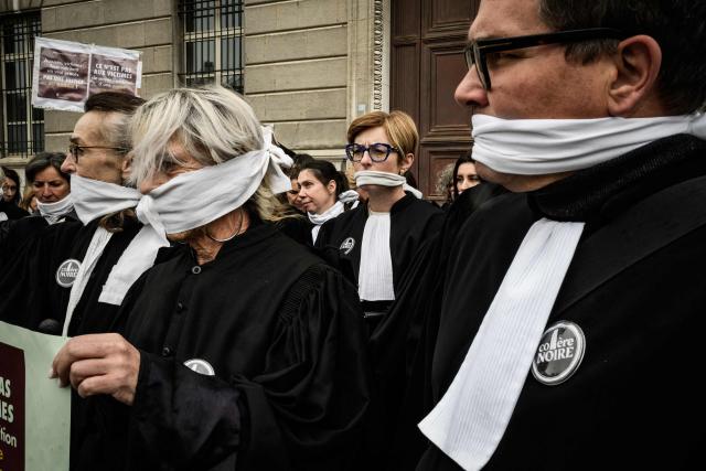 Lawyers gather with their mouths taped shut, in front of the Chambery courthouse, during a demonstration by lawyers against the "SURE" (Useful, Fast and Effective Sentencing) draft bill, in particular its proposal to introduce plea bargaining in criminal matters, as the French Senate begins debating the text, in Chambery on April 13, 2026. Lawyers across France staged a nationwide "Justice morte" (Dead Justice) stoppage called by most of the country's 164 bar associations, as the Senate opened debate on the bill which the government says is needed to tackle a backlog of more than 6,000 pending criminal cases. (Photo by JEFF PACHOUD / AFP)