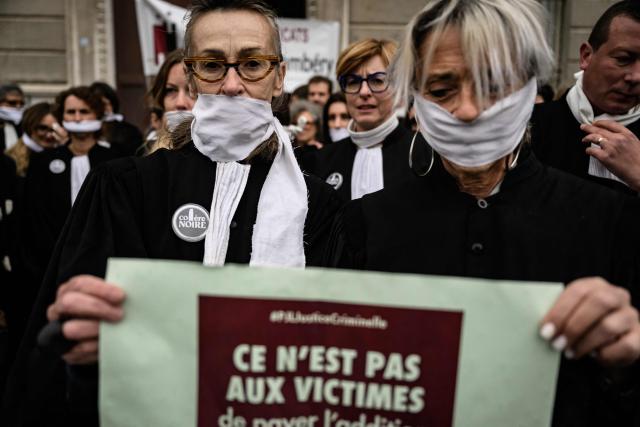 Lawyers gather with their mouths taped shut, in front of the Chambery courthouse, during a demonstration by lawyers against the "SURE" (Useful, Fast and Effective Sentencing) draft bill, in particular its proposal to introduce plea bargaining in criminal matters, as the French Senate begins debating the text, in Chambery on April 13, 2026. Lawyers across France staged a nationwide "Justice morte" (Dead Justice) stoppage called by most of the country's 164 bar associations, as the Senate opened debate on the bill which the government says is needed to tackle a backlog of more than 6,000 pending criminal cases. (Photo by JEFF PACHOUD / AFP)