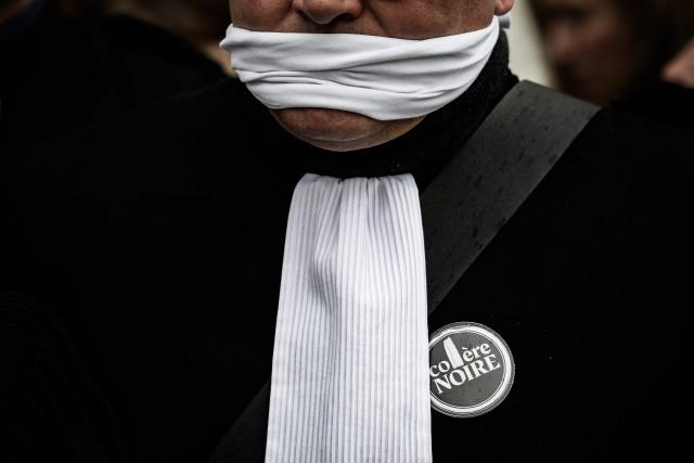 A lawyer with his mouth taped shut, takes part in a gathering in front of the Chambery courthouse, during a demonstration by lawyers against the "SURE" (Useful, Fast and Effective Sentencing) draft bill, in particular its proposal to introduce plea bargaining in criminal matters, as the French Senate begins debating the text, in Chambery on April 13, 2026. Lawyers across France staged a nationwide "Justice morte" (Dead Justice) stoppage called by most of the country's 164 bar associations, as the Senate opened debate on the bill which the government says is needed to tackle a backlog of more than 6,000 pending criminal cases. (Photo by JEFF PACHOUD / AFP)