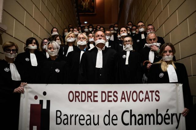 Lawyers gather with their mouths taped shut, in front of the Chambery courthouse, during a demonstration by lawyers against the "SURE" (Useful, Fast and Effective Sentencing) draft bill, in particular its proposal to introduce plea bargaining in criminal matters, as the French Senate begins debating the text, in Chambery on April 13, 2026. Lawyers across France staged a nationwide "Justice morte" (Dead Justice) stoppage called by most of the country's 164 bar associations, as the Senate opened debate on the bill which the government says is needed to tackle a backlog of more than 6,000 pending criminal cases. (Photo by JEFF PACHOUD / AFP)