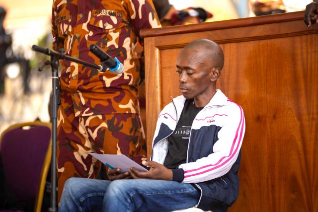 Christopher Okello Onyum, suspected in the killing of four toddlers at a daycare in Ggaba, stands in the dock during his trial at the Ggaba Community Church Grounds in Kampala on April 13, 2026. A man has admitted stabbing four young children to death at a kindergarten in Uganda, saying he believed killing them as human sacrifices would make him wealthy, prosecutors said April 8, 2026.
The public trial of the defendant, Christopher Okello Onyum, who holds both Ugandan and American citizenship, started on April 13, 2026. (Photo by Stuart Tibaweswa / AFP)