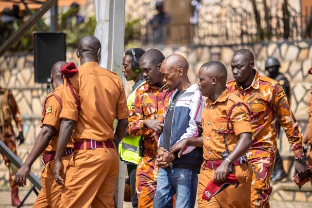 Christopher Okello Onyum (C), suspected in the killing of four toddlers at a daycare in Ggaba, is escorted Uganda Prison guards during his trial at the Ggaba Community Church Grounds in Kampala on April 13, 2026. A man has admitted stabbing four young children to death at a kindergarten in Uganda, saying he believed killing them as human sacrifices would make him wealthy, prosecutors said April 8, 2026.
The public trial of the defendant, Christopher Okello Onyum, who holds both Ugandan and American citizenship, started on April 13, 2026. (Photo by Stuart Tibaweswa / AFP)