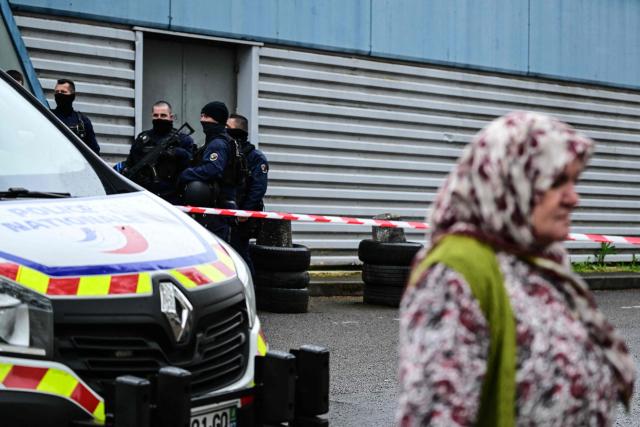 A pedestrian walks past as police officers secure a perimeter around the scene where a 13-year-old teenager was shot dead in the Belles Roches neighbourhood in Villefranche-sur-Saône, north of Lyon in southern central France, on April 13, 2026. Two minors aged 15 and 12 were taken into custody after the fatal shooting of a 13-year-old early afternoon in Villefranche-sur-Saône, prosecutors said, adding that an investigation for "murder" has been opened. (Photo by Olivier CHASSIGNOLE / AFP)