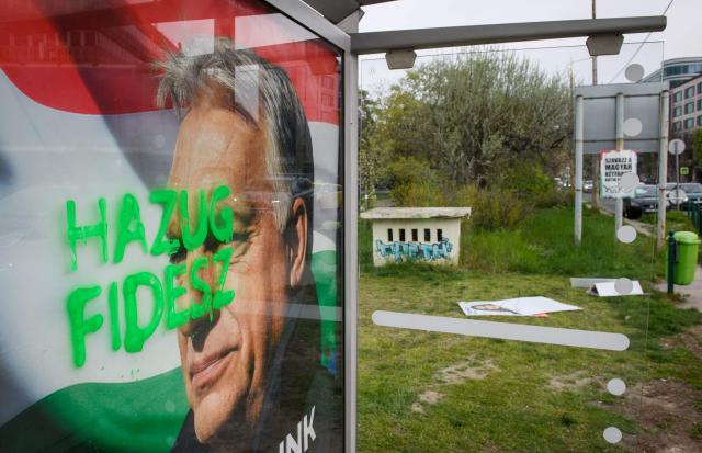 A tag reads 'Liar Fidesz' over a placard about a national petition against war, showing outgoing Hungarian Prime Minister and Fidesz leader Viktor Orban, at a bus stop near the South Railway Station, while election campaign posters lie scattered in the background, in Budapest, Hungary on April 13, 2026, one day after general elections. Hungarian prime minister-elect Peter Magyar pledged on April 13 to usher in a "new era" after defeating nationalist leader Viktor Orban in elections seen as a blow to hard-right populism. (Photo by Ferenc ISZA / AFP)