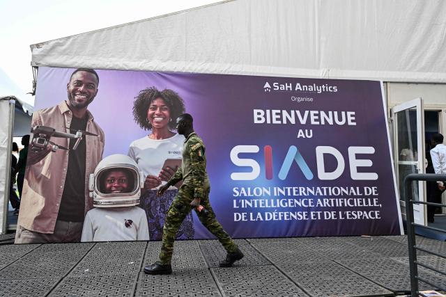 An Ivorian soldier walks past a banner for the 2nd edition of the International Exhibition on Artificial Intelligence, Defence and Space in Abidjan on April 13, 2026. (Photo by Issouf SANOGO / AFP)