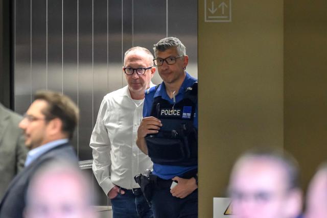 Mayor of Crans-Montana Nicolas Feraud (L) reacts as he is escorted by a police officer during a break of his hearing as part of the investigation over the fire that broke out in the bar "Le Constellation" during New Year celebrations, claiming 41 lives, most of them teenagers, and injuring 115 others, in Sion, western Switzerland, on April 13, 2026. (Photo by Fabrice COFFRINI / AFP)