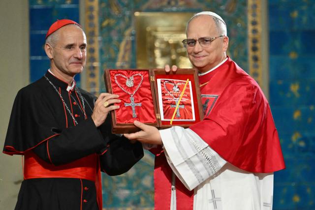 Pope Leo XIV receives a gift from the hands of cardinal Jean-Paul Vesco, Archbishop of Algiers, at the end of a meeting with the Algerian community in the Basilica of Our Lady of Africa, in Algiers on April 13, 2026. Pope Leo XIV embarks today on an 11-day visit to Algeria, Cameroon, Angola and Equatorial Guinea for his first major international trip since becoming pontiff last year. (Photo by Alberto PIZZOLI / AFP)