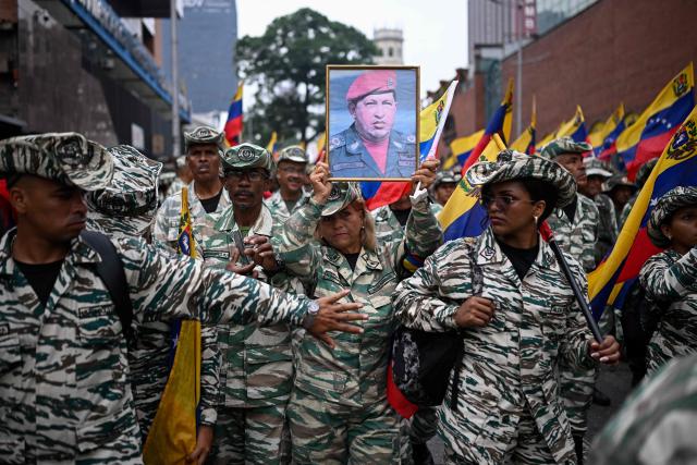 A member of the Bolivarian militia holds a portrait of late Venezuelan president Hugo Chavez (1999?2013) during a march marking his return to power after a failed 2002 coup, in Caracas on April 13, 2026. (Photo by Federico PARRA / AFP)