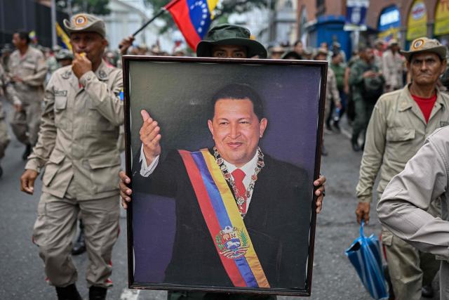 A member of the Bolivarian militia holds a portrait of late Venezuelan president Hugo Chavez (1999?2013) during a march marking his return to power after a failed 2002 coup, in Caracas on April 13, 2026. (Photo by Federico PARRA / AFP)