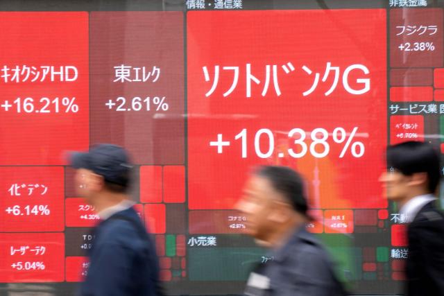 People walk past an electronic quotation board displaying stock price movements for various companies, including SoftBank Group (C), listed on the Tokyo Stock Exchange along a street in Tokyo on April 14, 2026. (Photo by Kazuhiro NOGI / AFP)