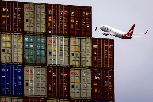 (FILES) A Qantas Airways Boeing 737 aircraft flies past containers stacked on a ship at the Port Botany terminal in Sydney on August 18, 2025. Surging jet fuel prices may raise costs for Australia's Qantas by up to Aus$800 million (US$570 million) in the second half of this year, the airline said April 14, 2026.
War in the Middle East has led jet fuel prices to more than double, and they remain "extremely volatile", the carrier said in a market update. (Photo by DAVID GRAY / AFP)