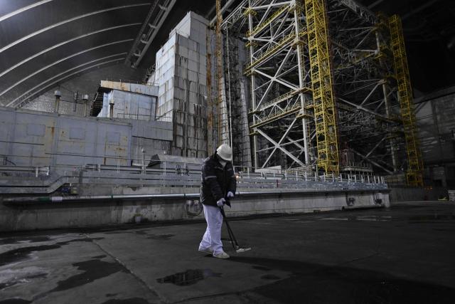 A radiation protection engineer works in front of the sarcophagus covering the destroyed fourth reactor under the New Safe Confinement (NSC), at the Chornobyl Nuclear Power Plant on April 9, 2026, amid the Russian invasion of Ukraine. An uncontrolled collapse of the internal radiation shell at the defunct Chernobyl nuclear power station in Ukraine could increase the risk of radioactivity release in the environment, Greenpeace warned on April 14, 2026. (Photo by Genya SAVILOV / AFP)