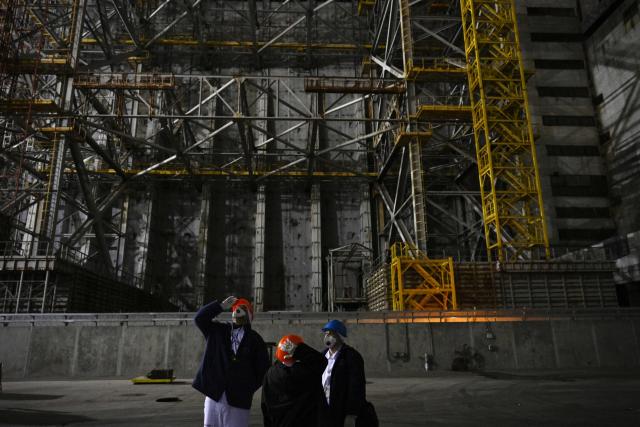 Visitors stand in front of the sarcophagus covering the destroyed fourth reactor under the New Safe Confinement (NSC), at the Chornobyl Power Plant on April 9, 2026, amid the Russian invasion of Ukraine. An uncontrolled collapse of the internal radiation shell at the defunct Chernobyl nuclear power station in Ukraine could increase the risk of radioactivity release in the environment, Greenpeace warned on April 14, 2026. (Photo by Genya SAVILOV / AFP)
