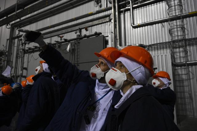 Representatives of Greenpeace and media stand in front of the sarcophagus covering the destroyed fourth reactor under the New Safe Confinement (NSC), at the Chornobyl Nuclear Power Plant on April 9, 2026, amid the Russian invasion of Ukraine. An uncontrolled collapse of the internal radiation shell at the defunct Chernobyl nuclear power station in Ukraine could increase the risk of radioactivity release in the environment, Greenpeace warned on April 14, 2026. (Photo by Genya SAVILOV / AFP)