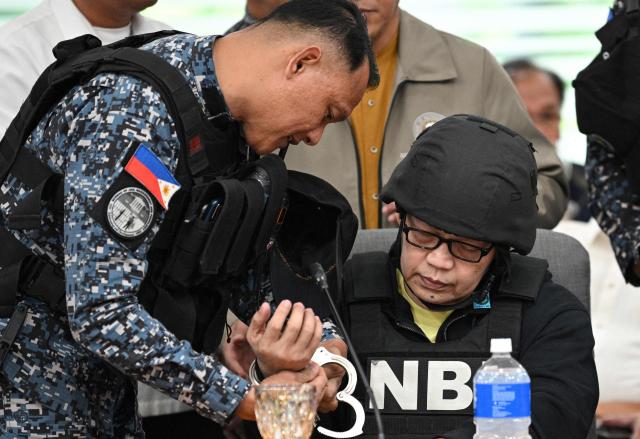 A member of the Bureau of jail management (L) removes the handcuffs off Ramil Madriaga (R) an alleged bagman of Philipine Vice-President Sara Duterte as he attends an impeachment hearing at the House of Representatives in Quezon City, suburban Manila on April 14, 2026. A Philippine congressional committee agreed overwhelmingly on March 4,to advance the impeachment case against Duterte, setting the stage for the poterntial vote that could decide her political future. (Photo by Ted ALJIBE / AFP)
