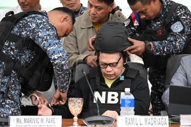 Members of the Bureau of jail management (L & R) remove the handcuffs and kevlar helmet off Ramil Madriaga (R) an alleged bagman of Philipine Vice-President Sara Duterte as he attends an impeachment hearing at the House of Representatives in Quezon City, suburban Manila on April 14, 2026. A Philippine congressional committee agreed overwhelmingly on March 4,to advance the impeachment case against Duterte, setting the stage for the poterntial vote that could decide her political future. (Photo by Ted ALJIBE / AFP)