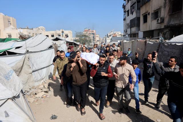 Palestinian mourners carry the shrouded body of Islam Quneita, a writer and managing editor for the website “Palestine Now,” who, according to medics, was killed in an Israeli strike the day before, past destroyed buildings and tents used as homes by displaced families during his funeral in Gaza City on April 14, 2026. Gaza is still reeling from more than two years of war between Israel and Hamas, sparked by the militant group's October 7, 2023, attack on Israel. (Photo by Omar AL-QATTAA / AFP)