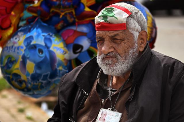 A street vendor hawking balloons sits with his face mask, in the colors of the Lebanese flag, lifted onto his forehead as he waits for customers along a street in Beirut on April 14, 2026. Israel said it was open to peace with Lebanon ahead of the first direct talks in decades between the neighbours on April 14, but that Hezbollah remained the "problem" blocking an agreement on ending fighting. (Photo by Joseph EID / AFP)