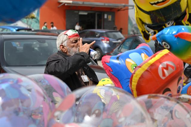 A street vendor hawking balloons sits with his face mask, in the colors of the Lebanese flag, lifted onto his forehead, as he sips a cup of tea waiting for customers along a street in Beirut on April 14, 2026. Israel said it was open to peace with Lebanon ahead of the first direct talks in decades between the neighbours on April 14, but that Hezbollah remained the "problem" blocking an agreement on ending fighting. (Photo by Joseph EID / AFP)