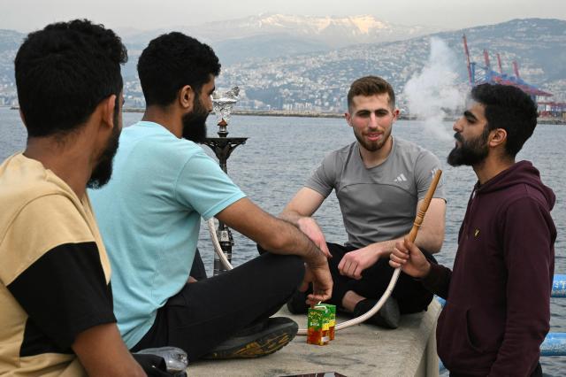 Men smoke a waterpipe as they sit by the sea near an unofficial camp for displaced people in Beirut's waterfront area on April 14, 2026. Israel said it was open to peace with Lebanon ahead of the first direct talks in decades between the neighbours on April 14, but that Hezbollah remained the "problem" blocking an agreement on ending fighting. (Photo by Joseph EID / AFP)