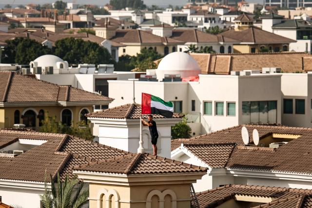 A man fixes the United Arab Emirates' national flag to the roof of his house in Dubai on April 14, 2026, after a call by the UAE’ Vice President, Prime Minister and Ruler of Dubai urging people across the country to hoist the flag as a symbol of unity and pride. (Photo by FADEL SENNA / AFP)