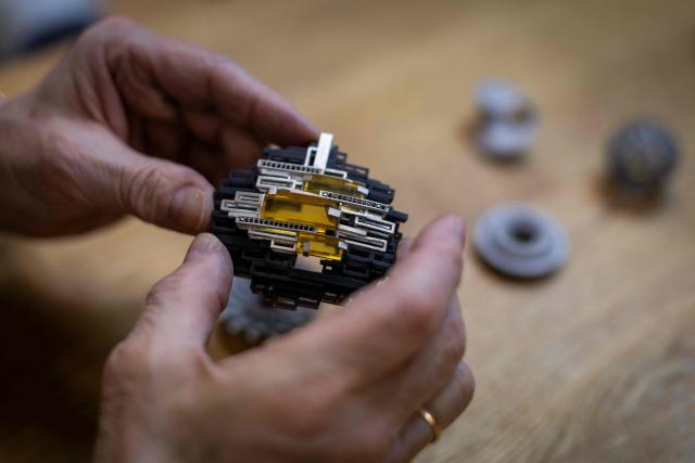 Marek Pawlowski, an amber jewellery creator, presents a piece of jewellery designed and created using 3D printing by a student from the Experimental Design Studio on Academy of Fine Arts in Gdansk, Poland on March 10, 2026. Long coveted for its golden color, scientific value and alleged healing properties, amber is now coming into the hand of young Polish jewelers, bringing the ancient resin into modern times. Together with drills, sanders, blasters, and power saws which look like they belong to a bygone era, virtual reality stations are used to combine earlier tools with state-of-the-art technology at the Academy of Fine Arts in Gdansk, a city on Poland's Baltic Coast known as amber's global capital. (Photo by Wojtek RADWANSKI / AFP)