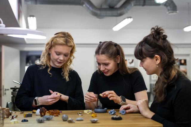 Martyna Golinska (C), and other students of the Experimental Design Studio lookss on pieces of jewellery design and created by other students on Academy of Fine Arts in Gdansk, Poland on March 10, 2026. Long coveted for its golden color, scientific value and alleged healing properties, amber is now coming into the hand of young Polish jewelers, bringing the ancient resin into modern times. Together with drills, sanders, blasters, and power saws which look like they belong to a bygone era, virtual reality stations are used to combine earlier tools with state-of-the-art technology at the Academy of Fine Arts in Gdansk, a city on Poland's Baltic Coast known as amber's global capital. (Photo by Wojtek RADWANSKI / AFP)
