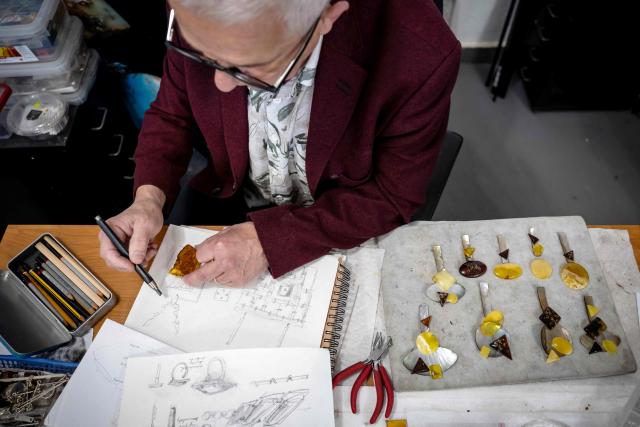 Jewellery designer Mariusz Gliwinski sketches a necklace design with a large piece of Baltic amber at his studio “Ambermoda”, in Sopot on March 27, 2026. Gliwinski’s company is one of 200 exhibitors at this year’s Amberif, a fair held annually in Gdansk where entrepreneurs, craftsmen and artists from all over the world who work with amber can sell or buy amber, establish new contracts or simply showcase their offerings. (Photo by Wojtek RADWANSKI / AFP)