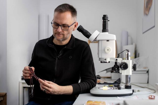 Michal Kosior, gemologist, amber specialist and founder of "Amber Expert", presents prayer beads made of glass meant to imitate amber, in his laboratory in Gdansk, northern Poland, on March 11, 2026. Formed some 40 million years ago from conifer resins, amber often contains air bubbles, plant fragments or insects trapped before fossilisation, granting each piece a unique "fingerprint". In Gdansk itself, workshops, shops and stalls dedicated to amber abound on every corner of the historic centre, each attracting flocks of tourists. (Photo by Wojtek RADWANSKI / AFP)