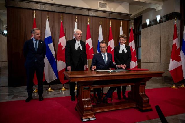 Canadian Prime Minister Mark Carney (L) looks on as Finland's President Alexander Stubb signs the guest book at Parliament Hill in Ottawa, Canada on April 14, 2026. (Photo by ANDREJ IVANOV / AFP)