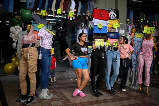 Women rest on mannequins in a clothing store outside a courthouse in Caracas on April 14, 2026. (Photo by Federico PARRA / AFP)