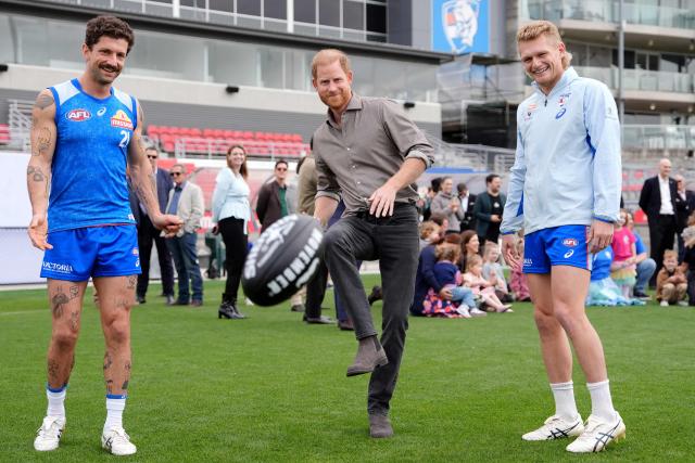 Britain's Prince Harry, Duke of Sussex (C), kicks a ball with Western Bulldogs Australian Football League (AFL) players Tom Liberatore (L) and Adam Treloar (R) during a visit to a Movember event at Whitten Oval in Melbourne on April 15, 2026. (Photo by Jonathan Brady / POOL / AFP)