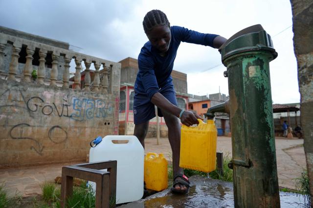 (FILES) A young man fills a water barrel at a payment-operated water fountain, in Tsoundzou 2 district, in the township of Mamoudzou, on the French Indian Ocean territory of Mayotte, on October 31, 2025. For three years now, the taps in Mayotte have been running only intermittently. As the Paris criminal court delivers its ruling on April 16, 2026 in the trial of the former management of the water authority, the people of Mayotte are enduring scheduled water cuts, the legacy of a historic drought in 2023, but also of poor management and exhausted infrastructure. (Photo by Marine GACHET / AFP)