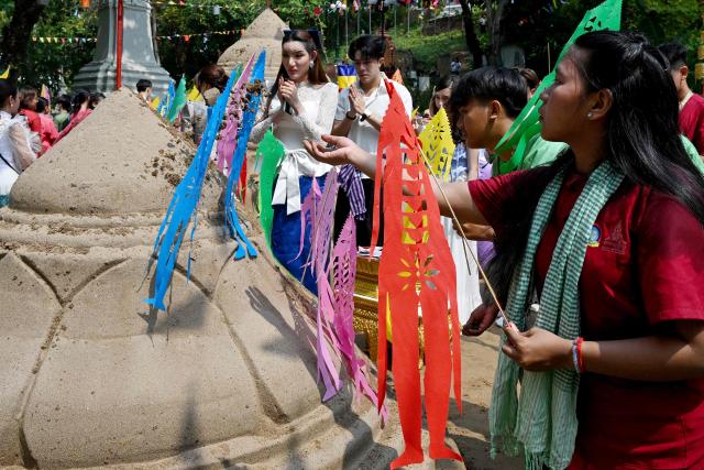 A woman throws sand on sand stupas as they pray during celebrations for the Khmer New Year, known as Nokor Sankranta, in Phnom Penh on April 15, 2026. (Photo by TANG CHHIN Sothy / AFP)
